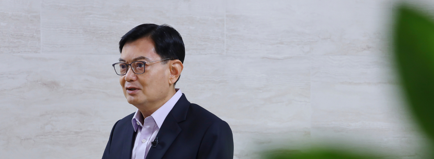 Heng Swee Keat wearing glasses and a suit, speaking in front of a textured wall.